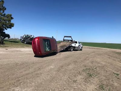 A red car is being towed by a tow truck on a dirt road.
