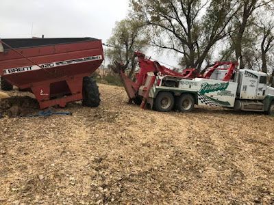 A tow truck is towing a combine harvester in a field.