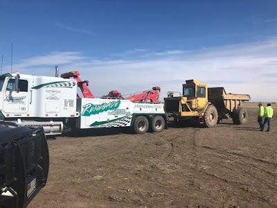 A tow truck is towing a dump truck in a dirt field.