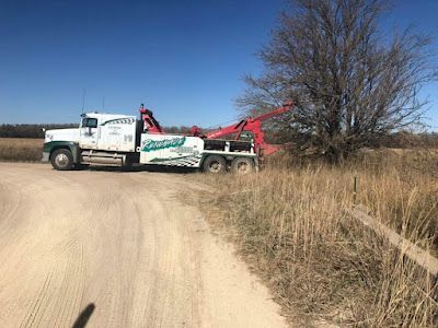 A tow truck is driving down a dirt road next to a field.