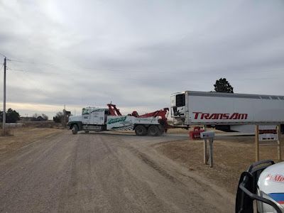 A tow truck is towing a semi truck down a dirt road.