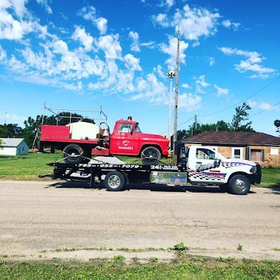 A tow truck with a red truck on the back is parked on the side of the road.