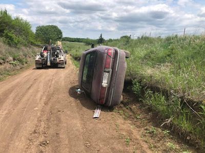 A car is on its side on a dirt road being towed by a tow truck.