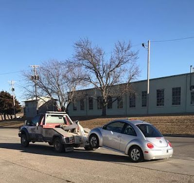 A silver car is being towed by a tow truck.