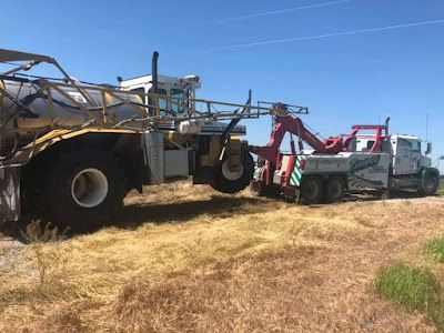 A tow truck is towing a tractor in a field.