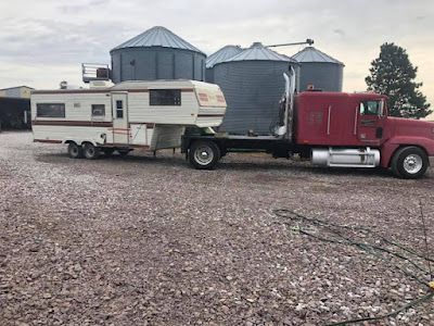 A red semi truck is towing a trailer in a gravel lot.