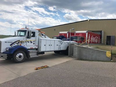 A tow truck is parked in front of a coca cola truck.
