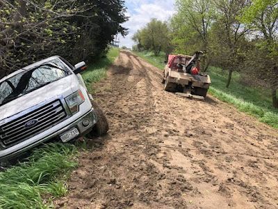 A white truck is stuck in the mud on a dirt road.