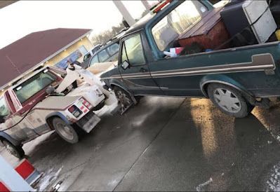 A truck is being towed by a tow truck at a gas station