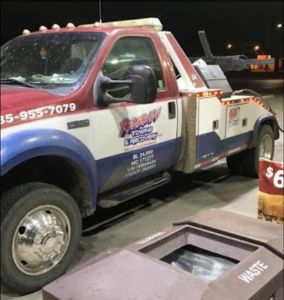 A red white and blue tow truck is parked next to a waste bin