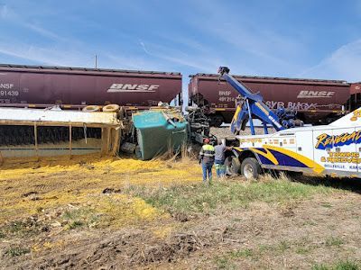 A tow truck is towing a train car that has fallen off the tracks.