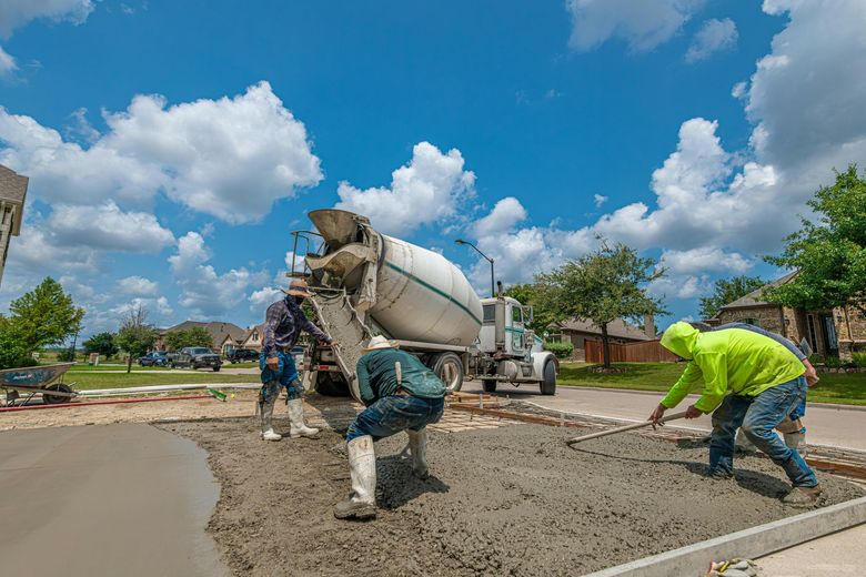 Construction workers pouring concrete from a truck, leveling it on a sunny day.