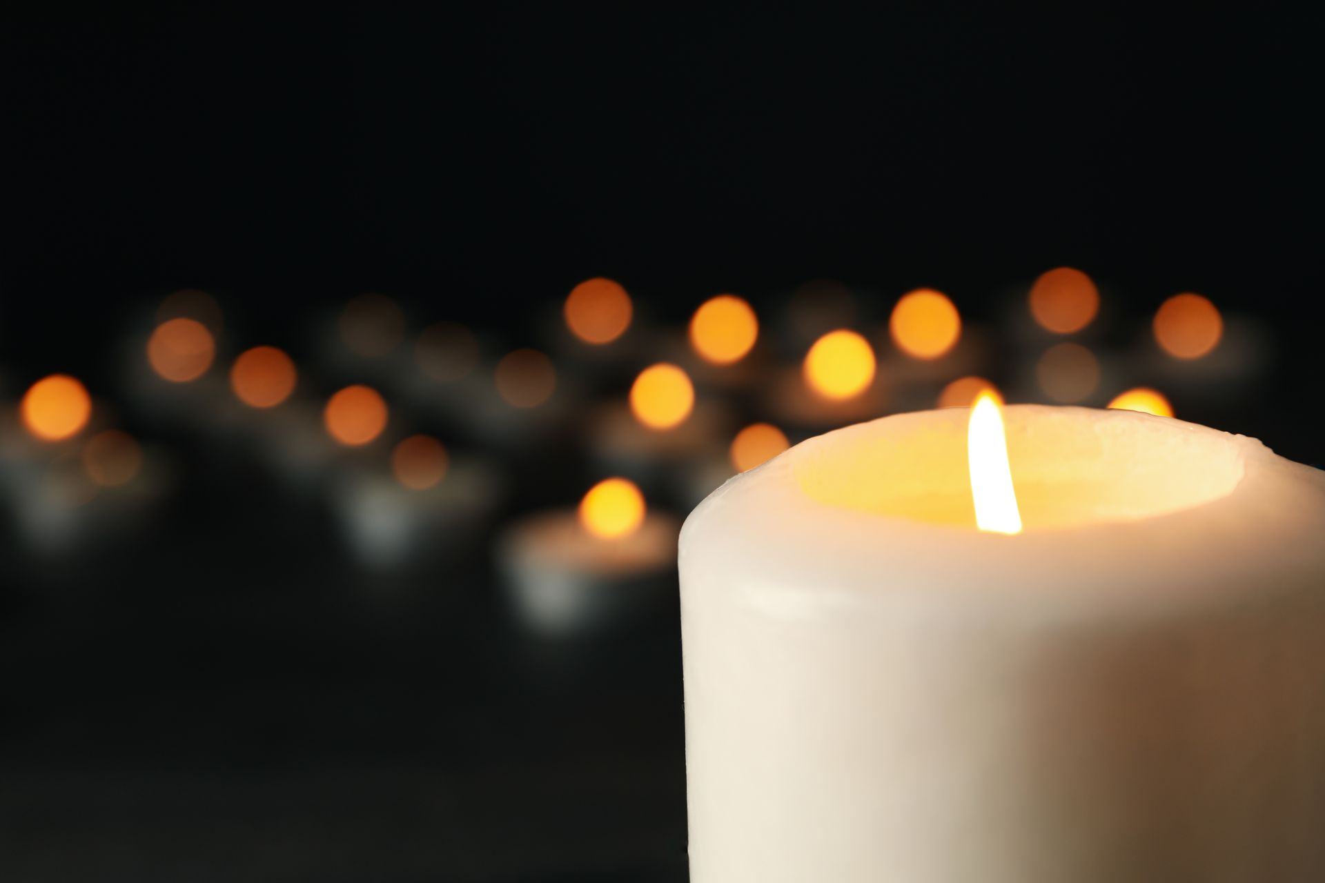 Vor einer Reihe brennender Kerzen wird eine weiße Kerze angezündet.