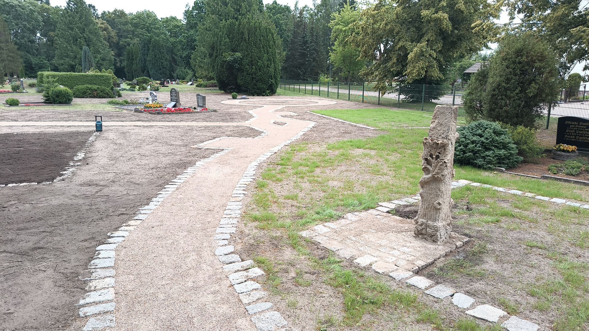Ein Friedhof mit einem hindurchführenden Weg und Bäumen im Hintergrund.