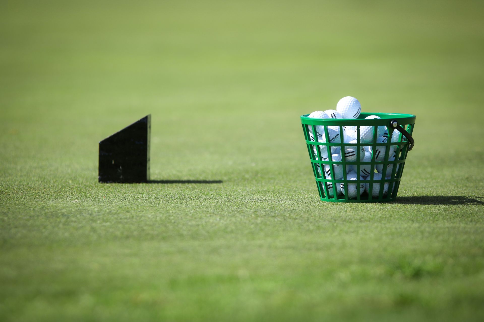 A green basket filled with golf balls is on a golf course.