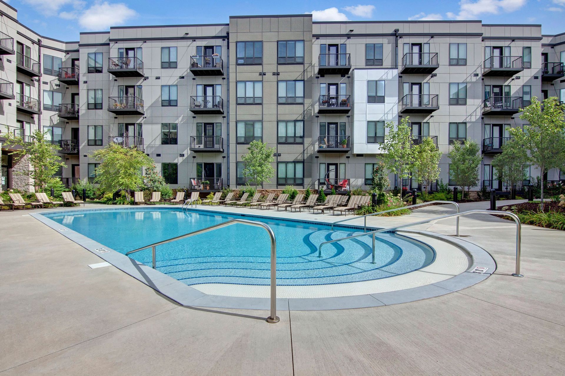 Modern The Residence at The COR Apartment Homes complex surrounds a serene outdoor pool with inviting lounge chairs and lush greenery under a clear blue sky.