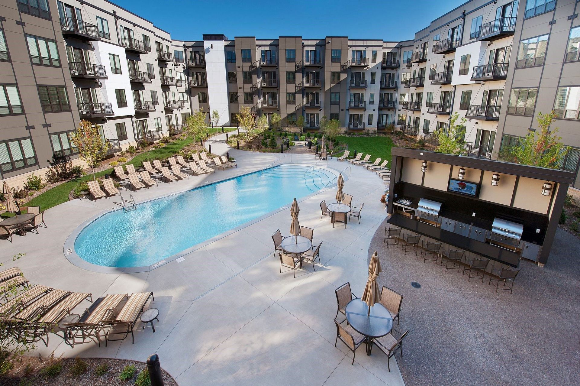 Modern courtyard here at The Residence at The COR Apartment Homes with a swimming pool surrounded by sun loungers and patio tables with umbrellas. Grills and seating area create a relaxing vibe.