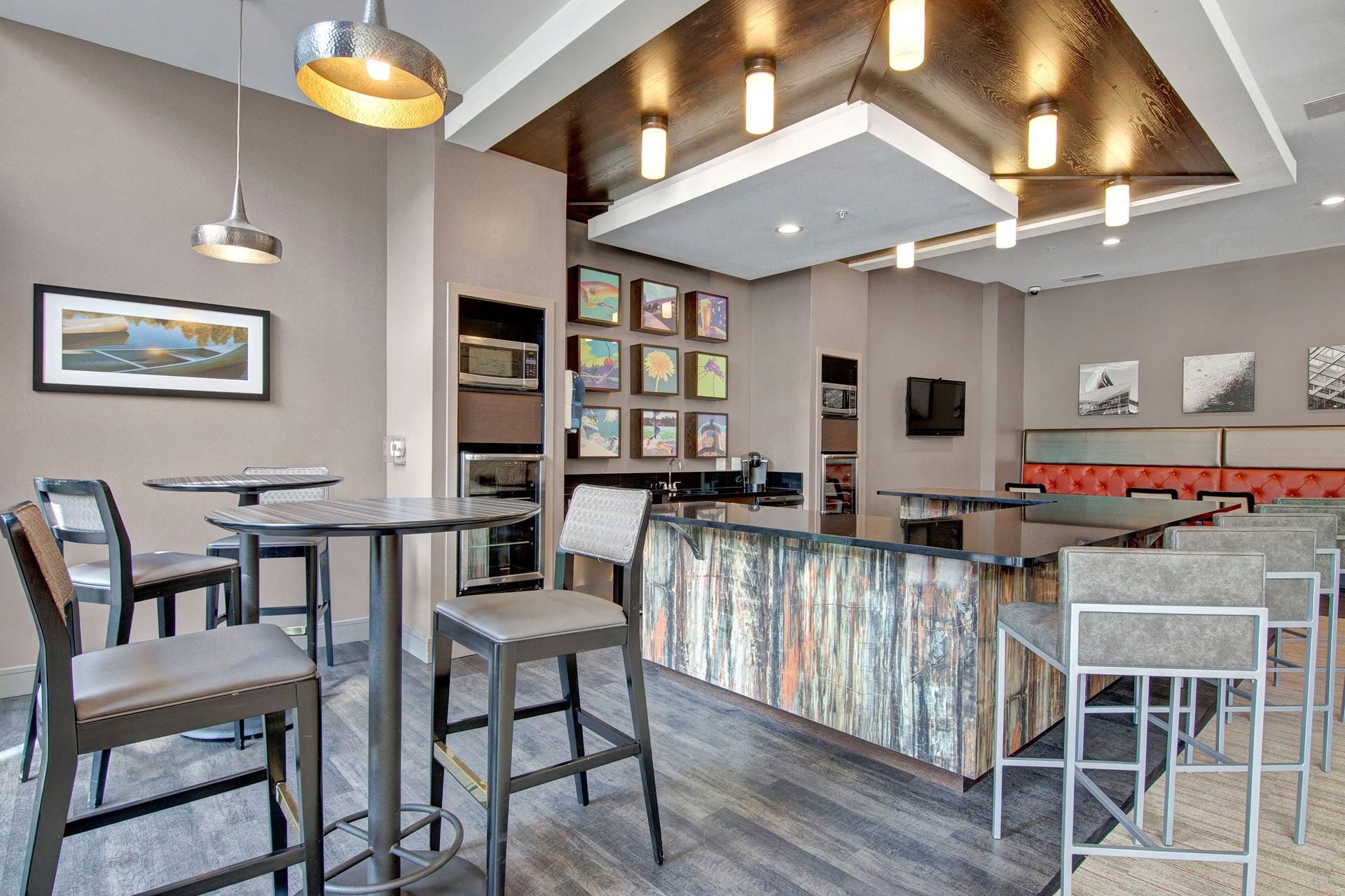 Modern lounge area here at The Residence at The COR Apartment Homes with high tables and chairs, pendant lighting, a textured bar, colorful artwork, and a wall-mounted TV, creating a cozy, inviting atmosphere.
