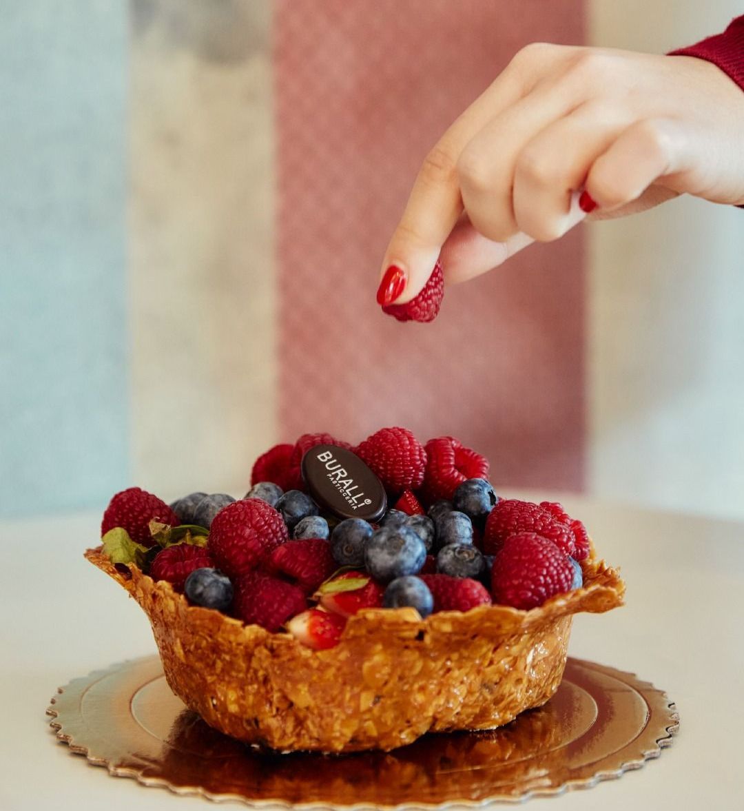 Una persona sta mettendo una fragola sopra una torta di frutti di bosco