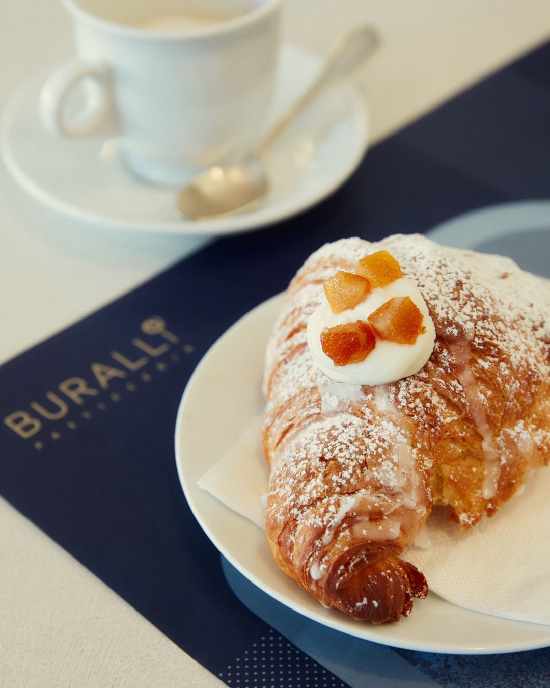Un croissant su un piatto con zucchero a velo accanto a una tazza di caffè