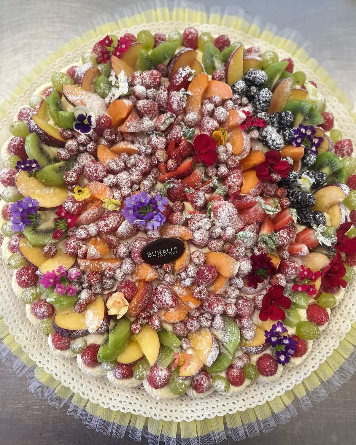 Una torta con tanta frutta e fiori sopra
