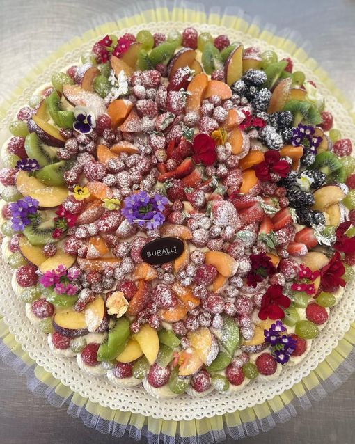 Una torta con tanta frutta e fiori sopra