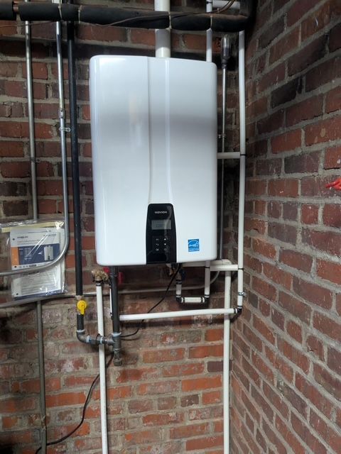 A white water heater is mounted to a brick wall