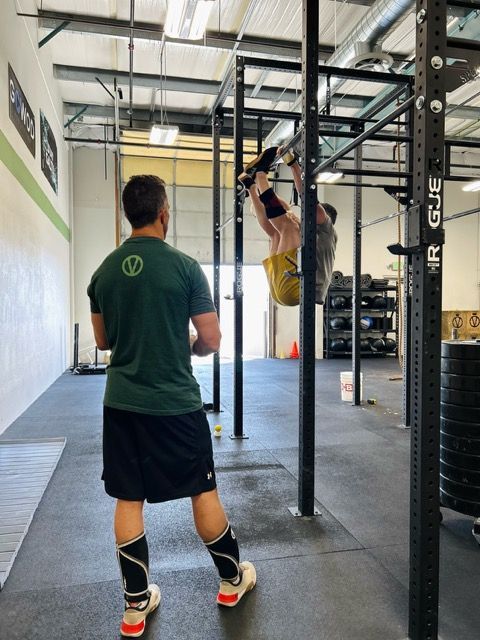 A man watches another doing a hanging knee raise on a pull-up bar at Verdant CrossFit in Boise.