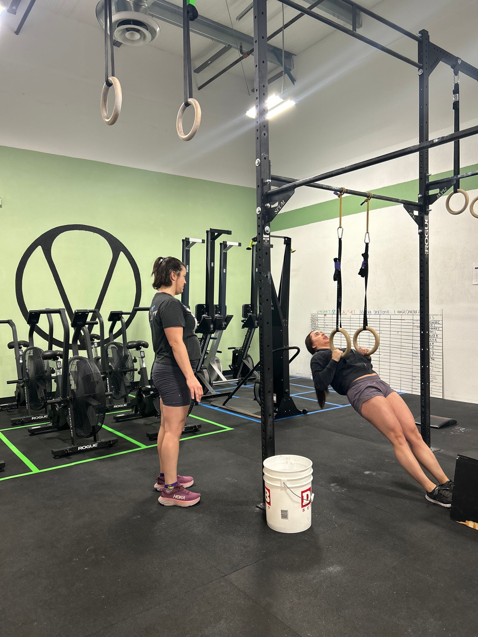 Woman doing ring rows at Verdant CrossFit in Boise, observed by another woman.