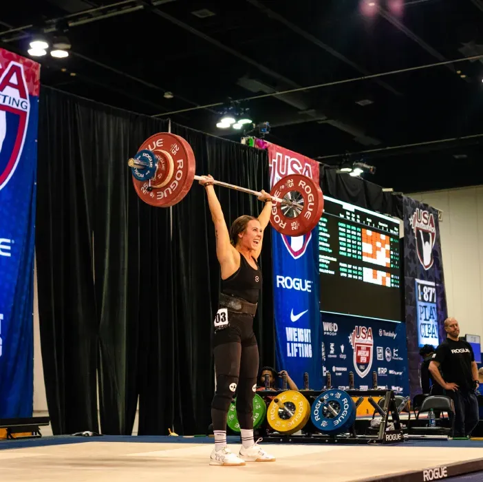 Weightlifter in black singlet overhead presses barbell at USA Weightlifting event.
