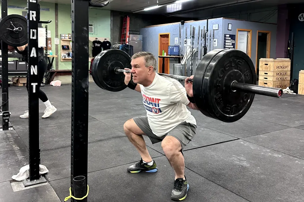 Man squatting with a heavy barbell at Verdant CrossFit gym in Boise, wearing a white t-shirt and gray shorts.