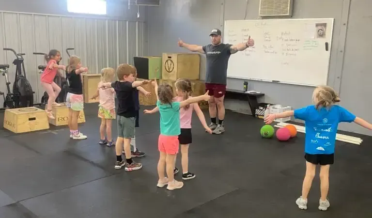 Group of children in a gym in Boise, ID, arms out, following instructor's demonstration.