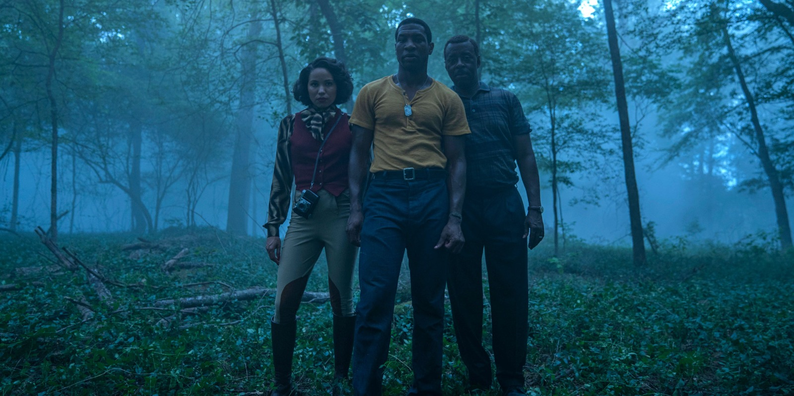 Lovecraft Country characters Leti, Tic, and George standing in a misty forest at dusk.