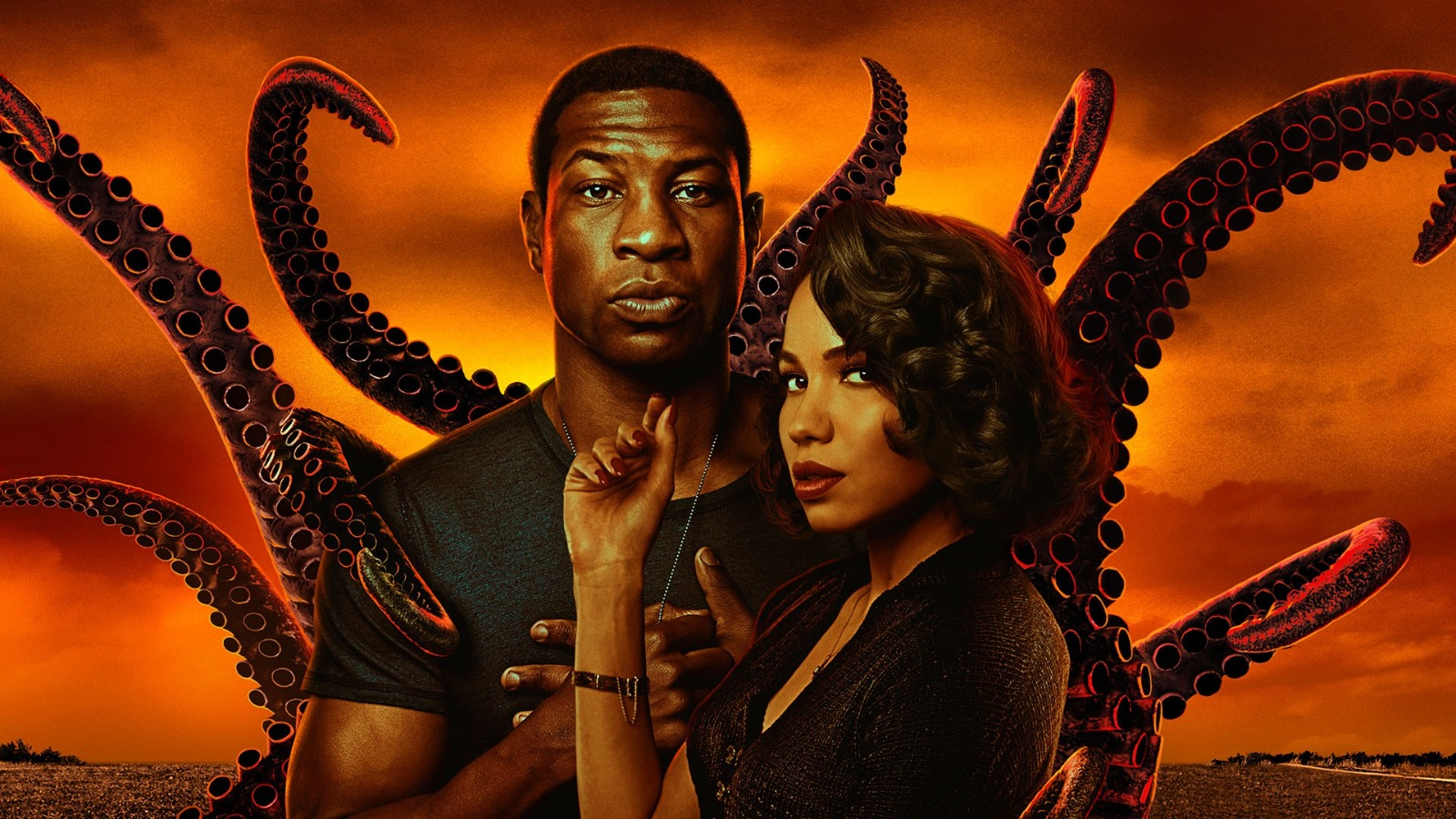 A black man and woman stand before an orange sunset with looming tentacles in the background. Lovecraft Country Misha Green