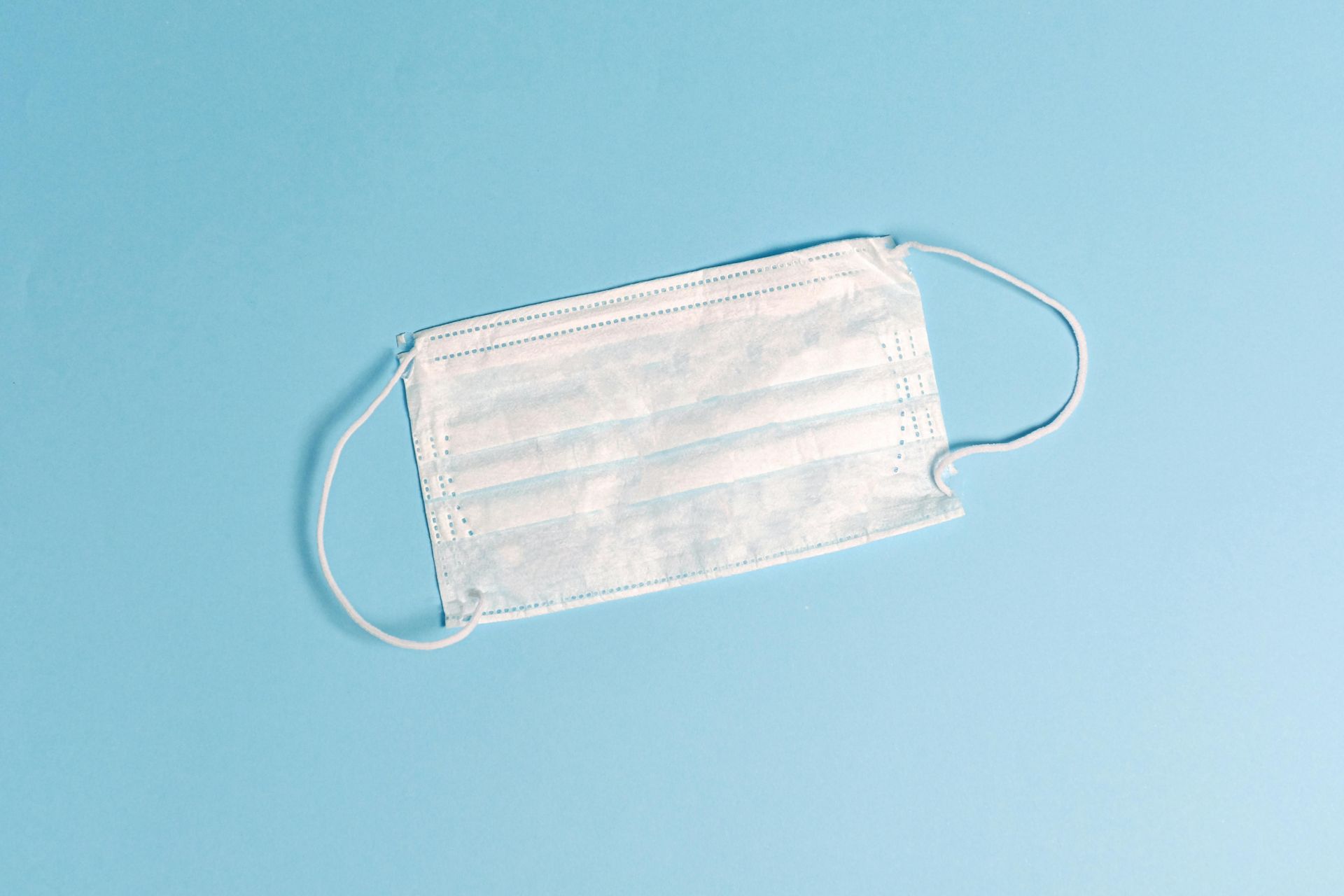White disposable medical mask against a blue background