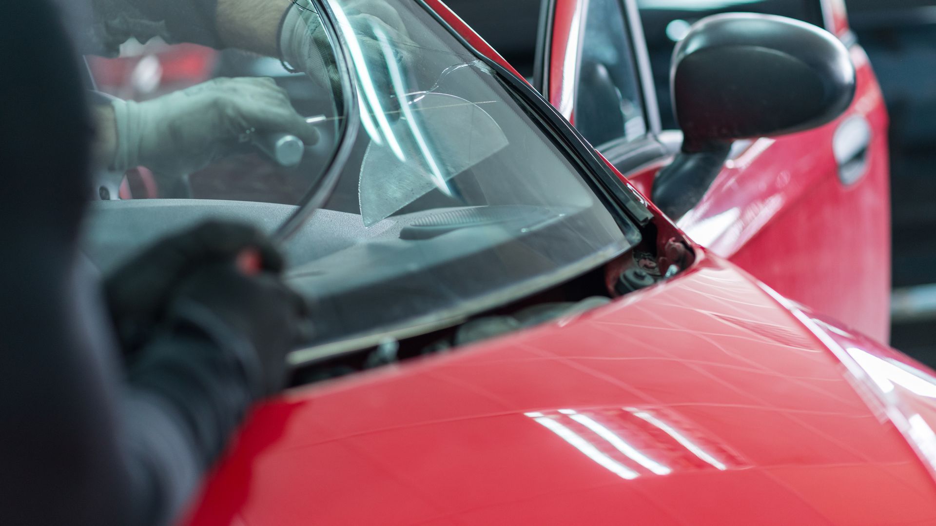 Hands in black gloves removing a windshield from a red car.