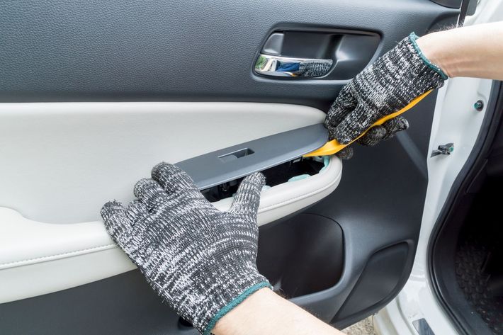 Hands wearing gloves using a tool to remove a panel from a car door.