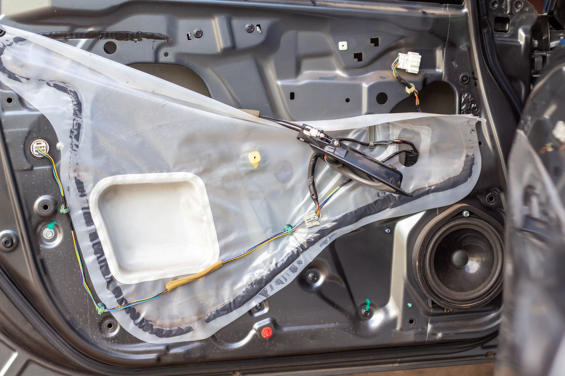 Car door interior with the door panel removed, showing speaker, wiring, and vapor barrier.