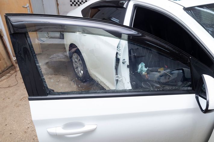 A white car with the front door open, showcasing a tinted window and black rain guard.