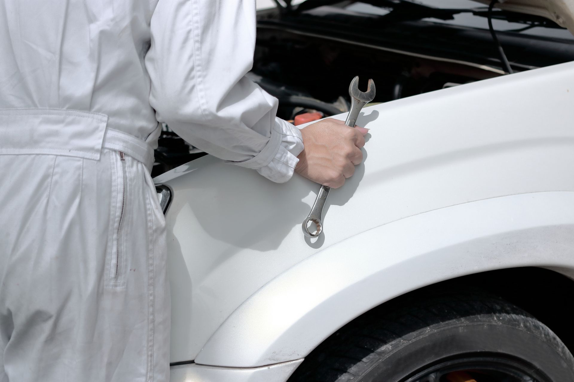 Mechanic in white coveralls holding a wrench, working on a white car.