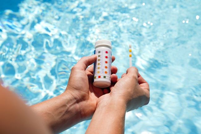 A person is holding a test kit in their hands in front of a swimming pool.