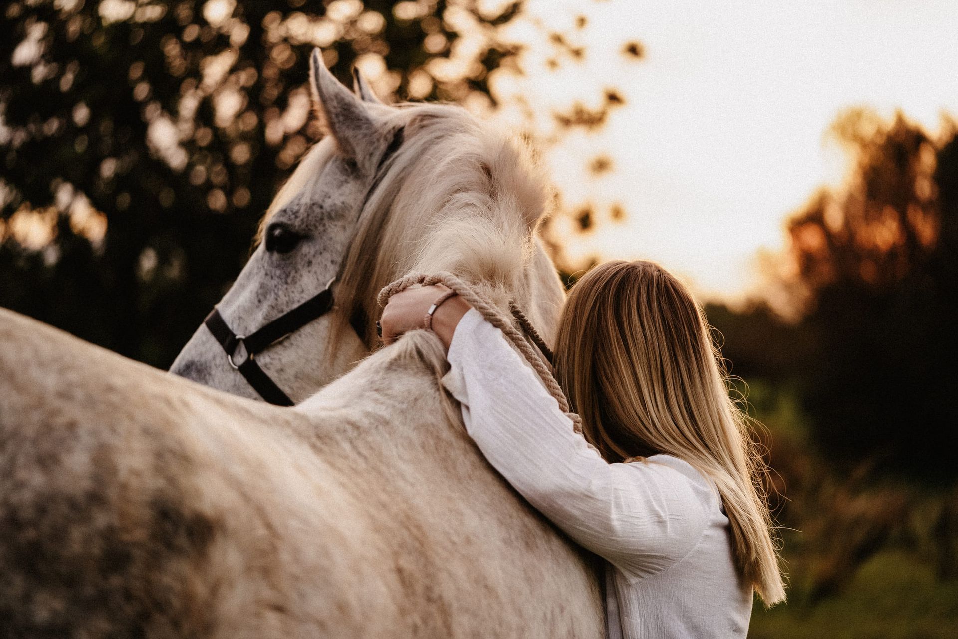A woman is hugging a white horse in a field.