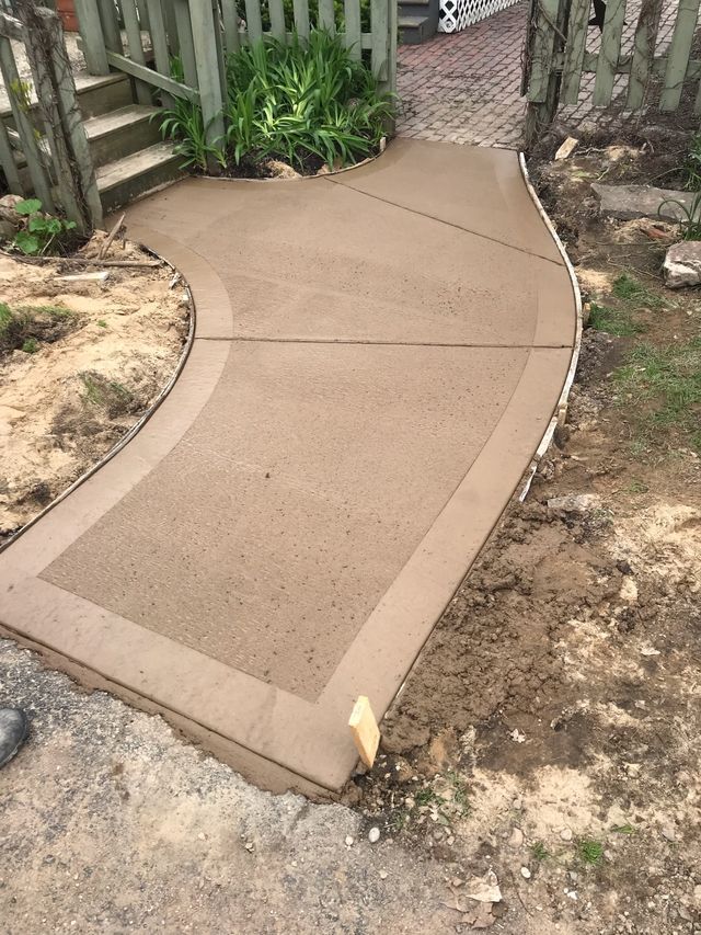 A concrete walkway is being built next to a fence.