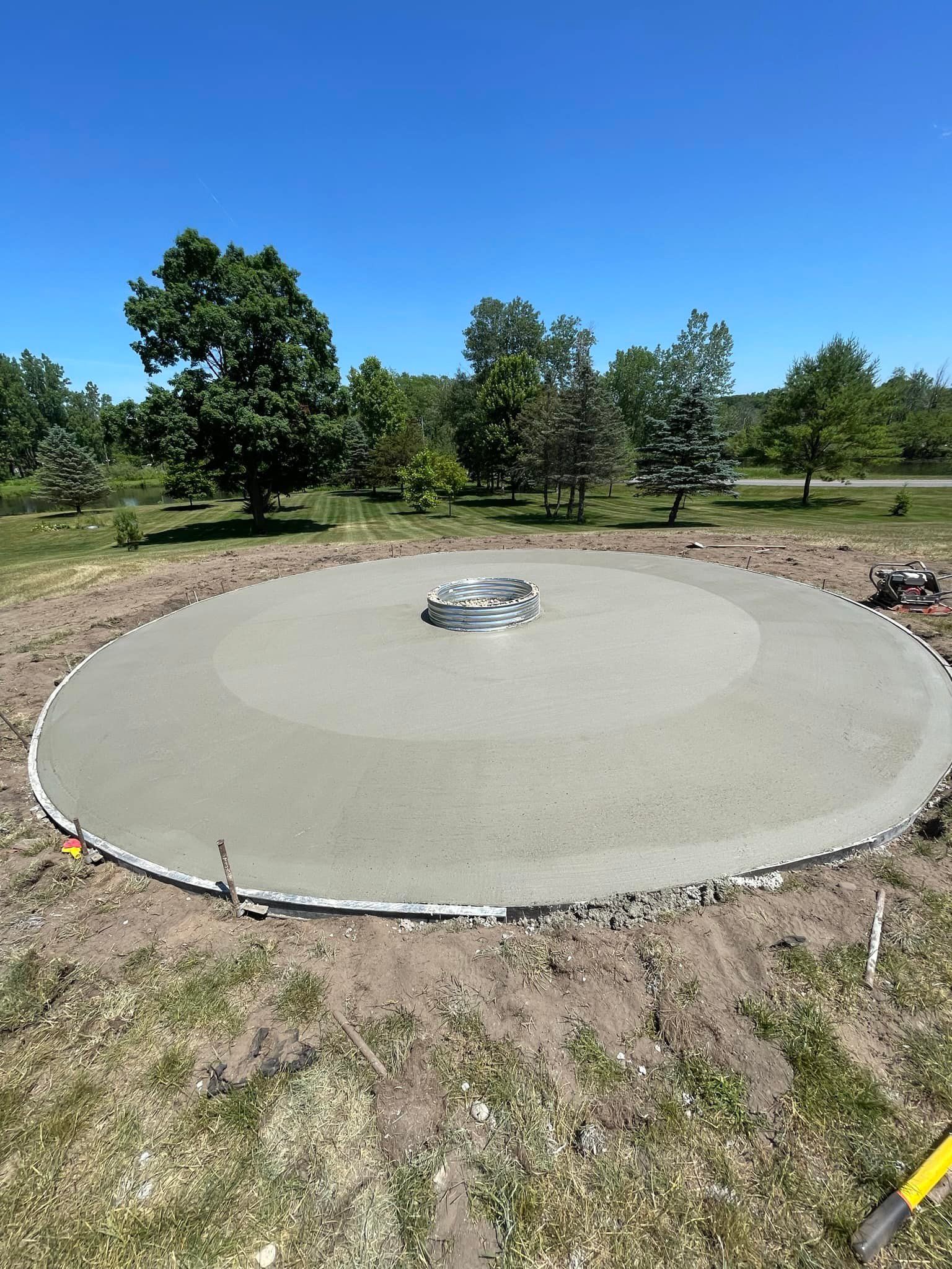 A large circle of concrete is being poured in a field with trees in the background.