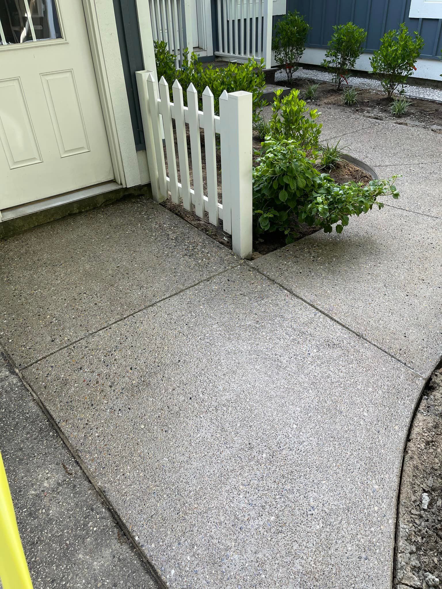 A concrete walkway with a white picket fence in front of a house.