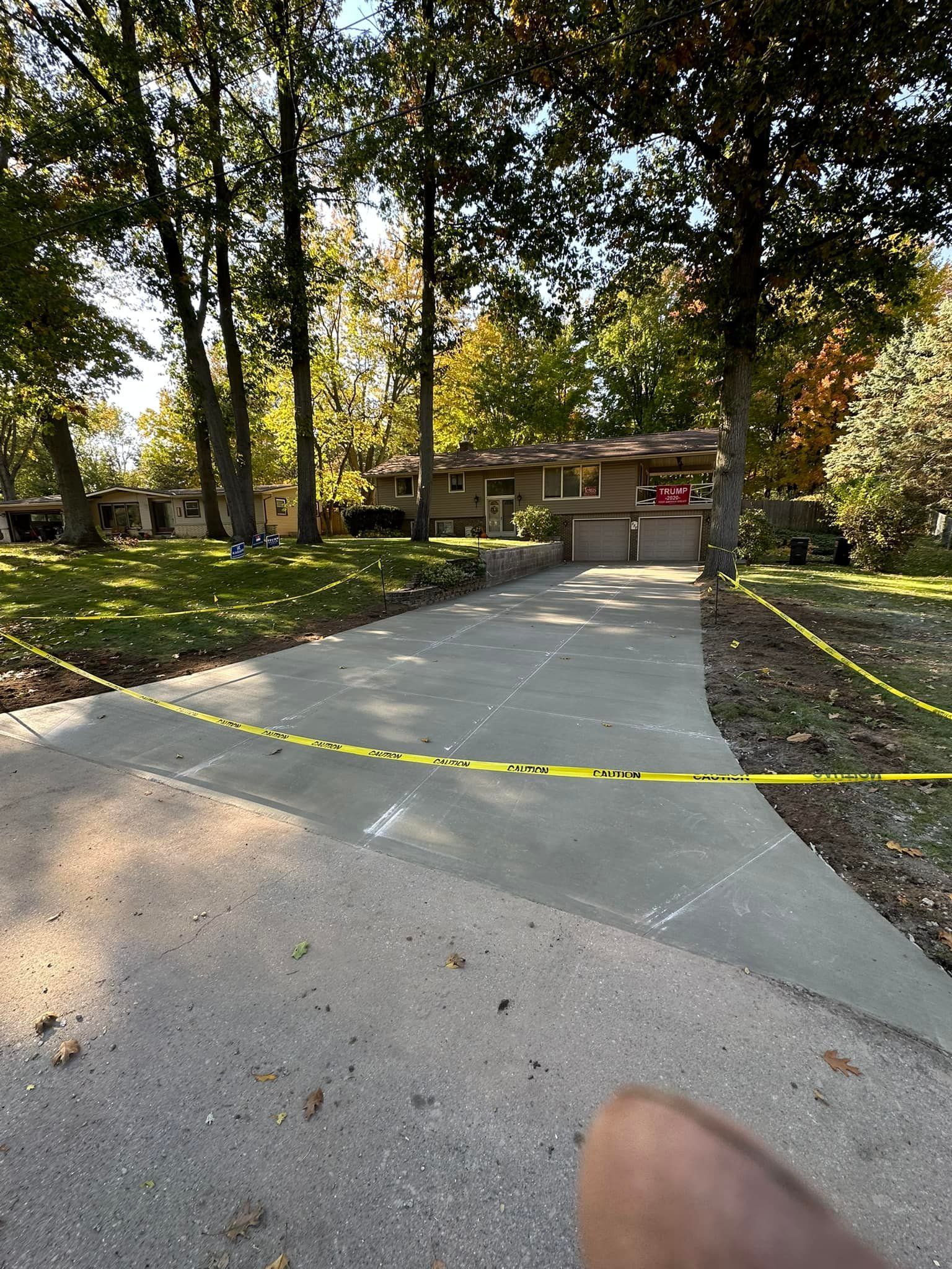 A person is standing on a concrete driveway in front of a house.