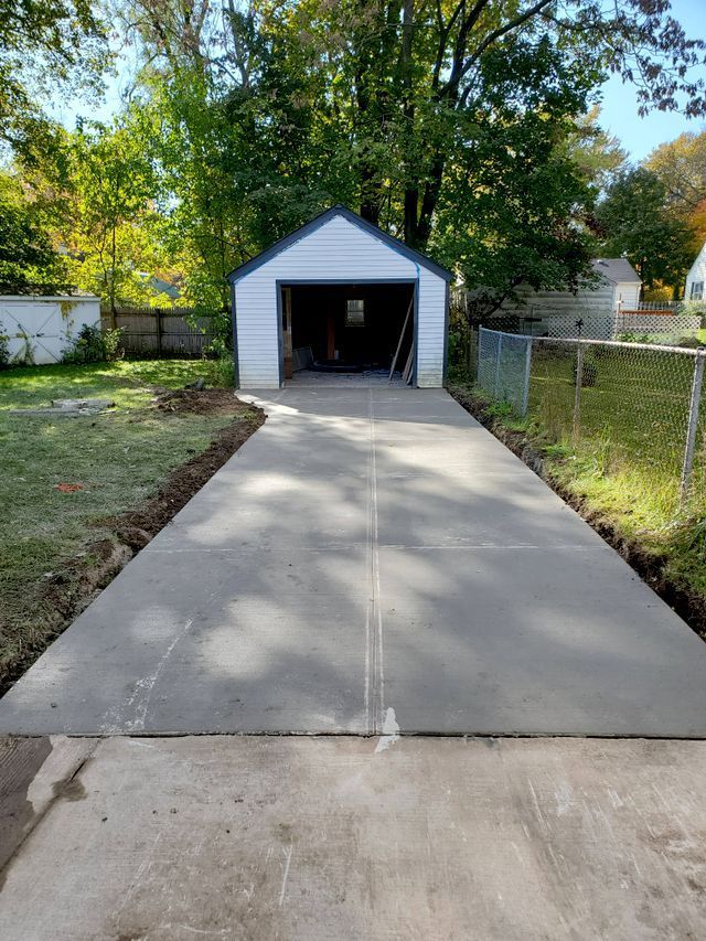 A concrete driveway leading to a garage with a shed in the background.