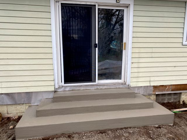 A house with a sliding glass door and concrete steps leading to it.