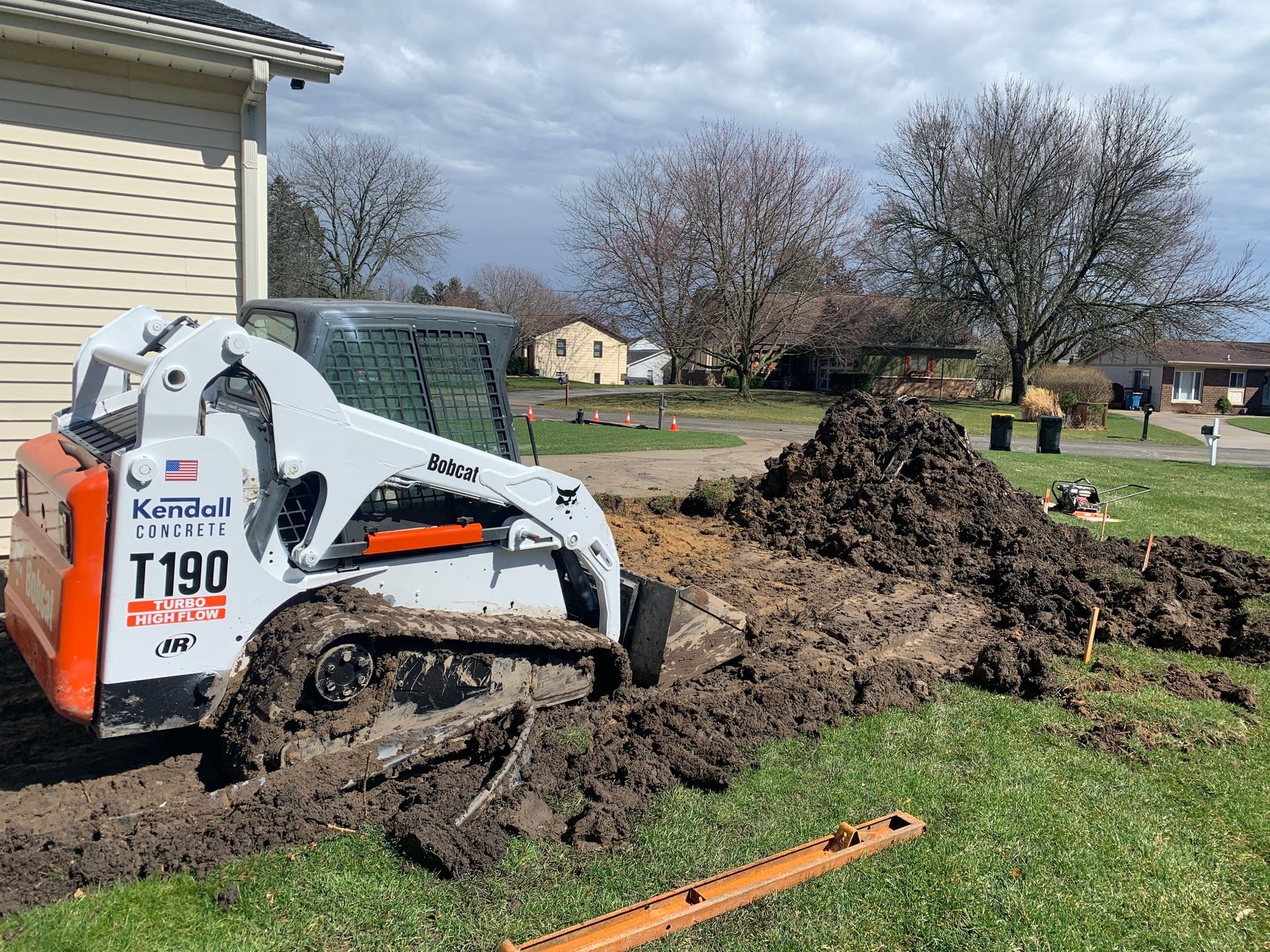 A bulldozer is digging a hole in the dirt in front of a house.