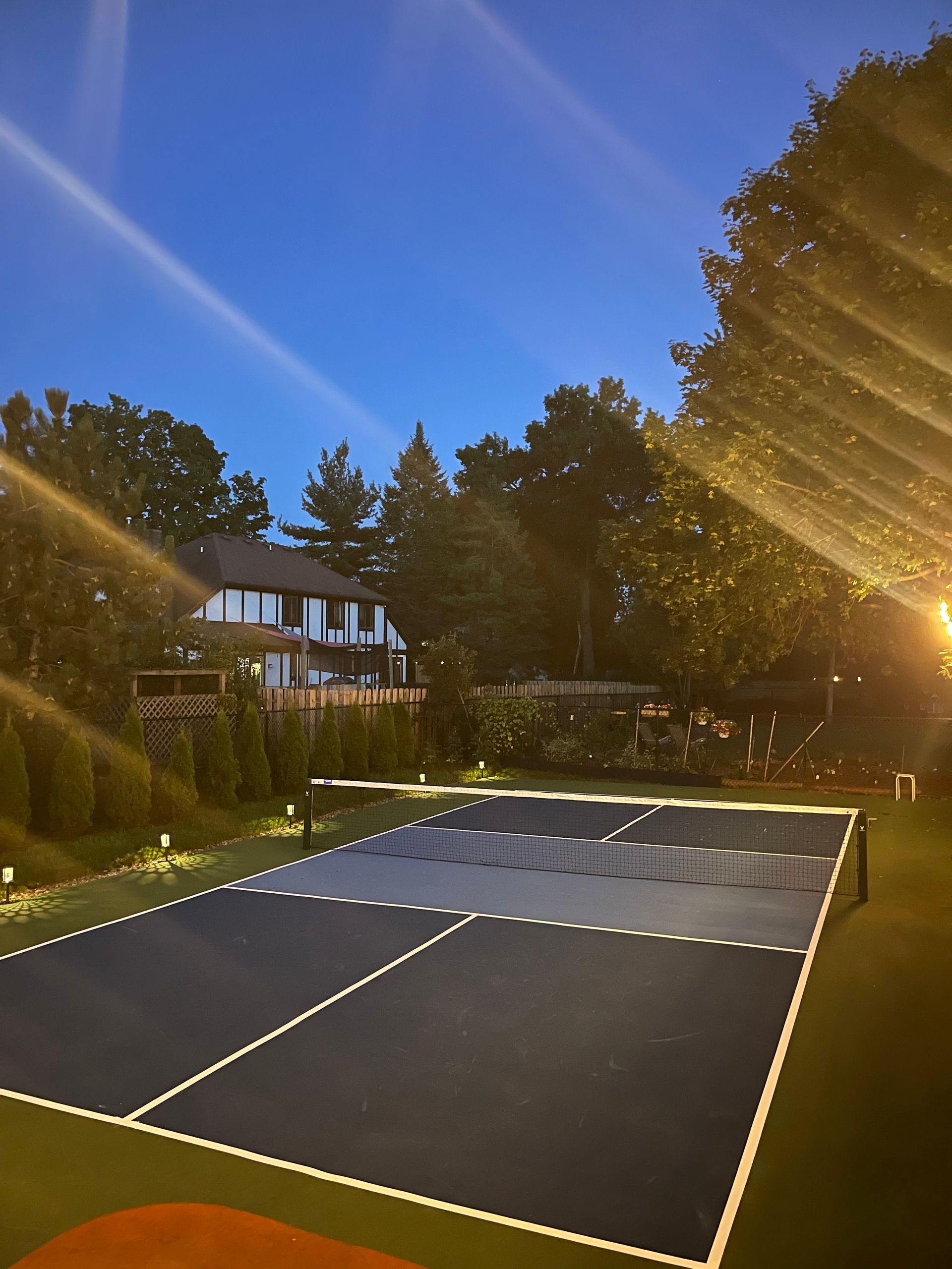 A tennis court is lit up at night with a house in the background